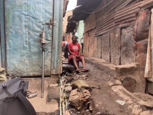 A local women in Mathare sitting down on a step next to a narrow pathway between two houses