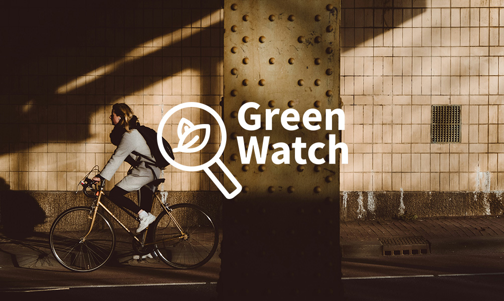 Women cycling along a street with the Green Watch logo in the forground