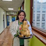 Sophia van Mourik in a lab coat holding a teddy bear cake