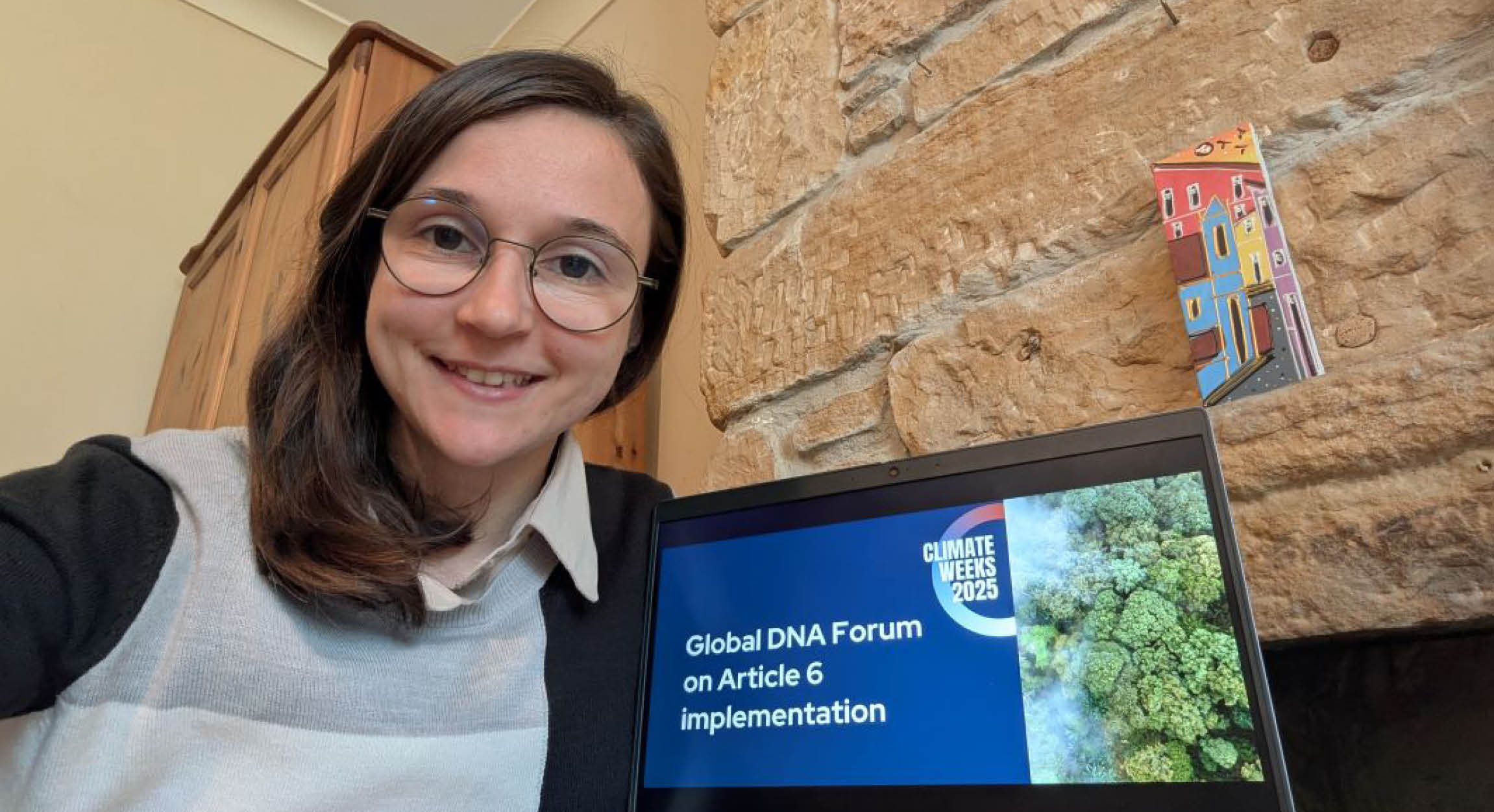 Issi Steeley sat in front of a laptop with the title "Global DNA Forum on Article 6 Implementation' displayed on the screen