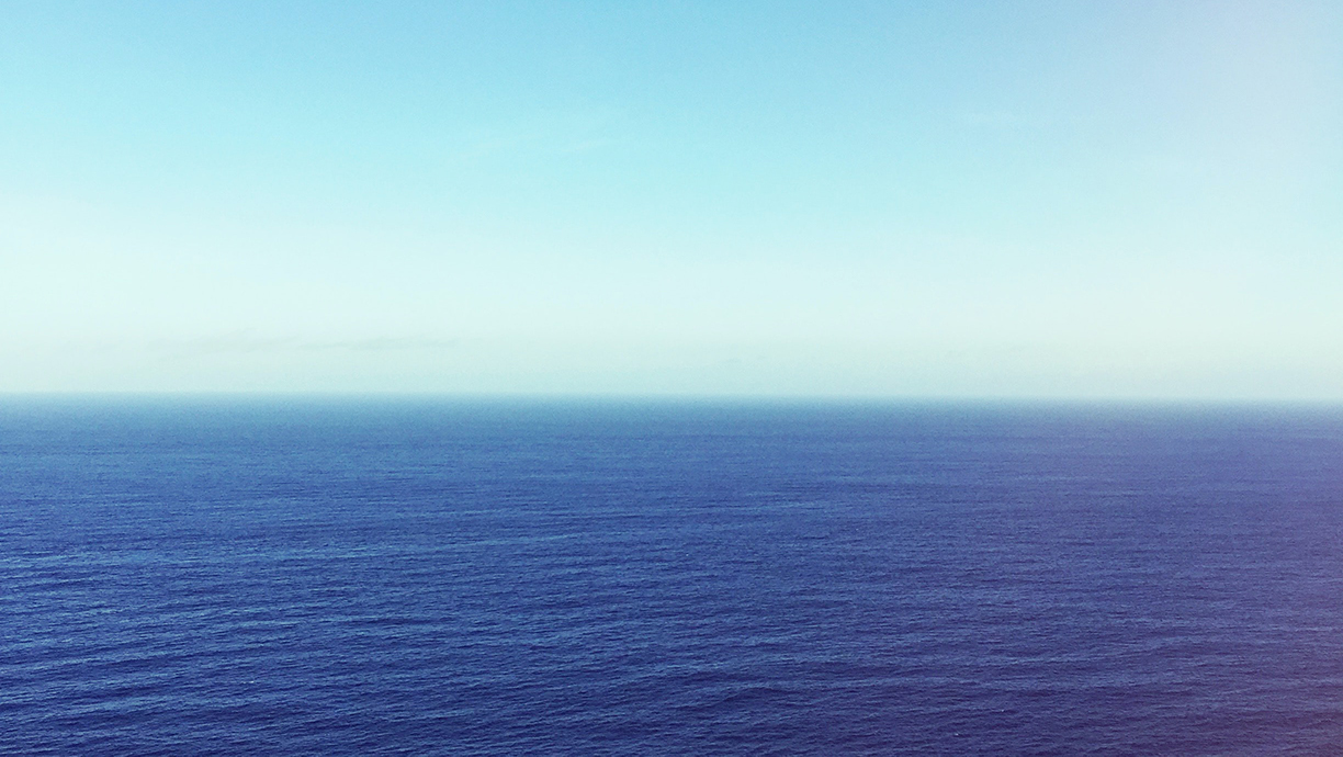Photo of blue sky and darker blue ocean stretching to the horizon.