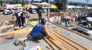 Three builders working on the roof of the sustainable cold room. They are measuring out wooden beams