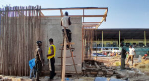 One builder standing on a ladder next to the sustainable cold room while two other people stand nearby